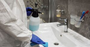 A person sanitizing a bathroom sink with a spray bottle, ensuring hygiene.